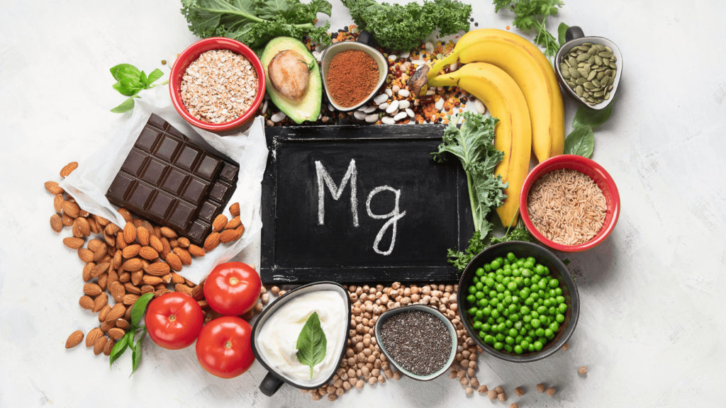 Comida como plátanos, tomates, legumbres, guisantes, chocolates esparcidos en una mesa con las siglas Mg en medio, de magnesio