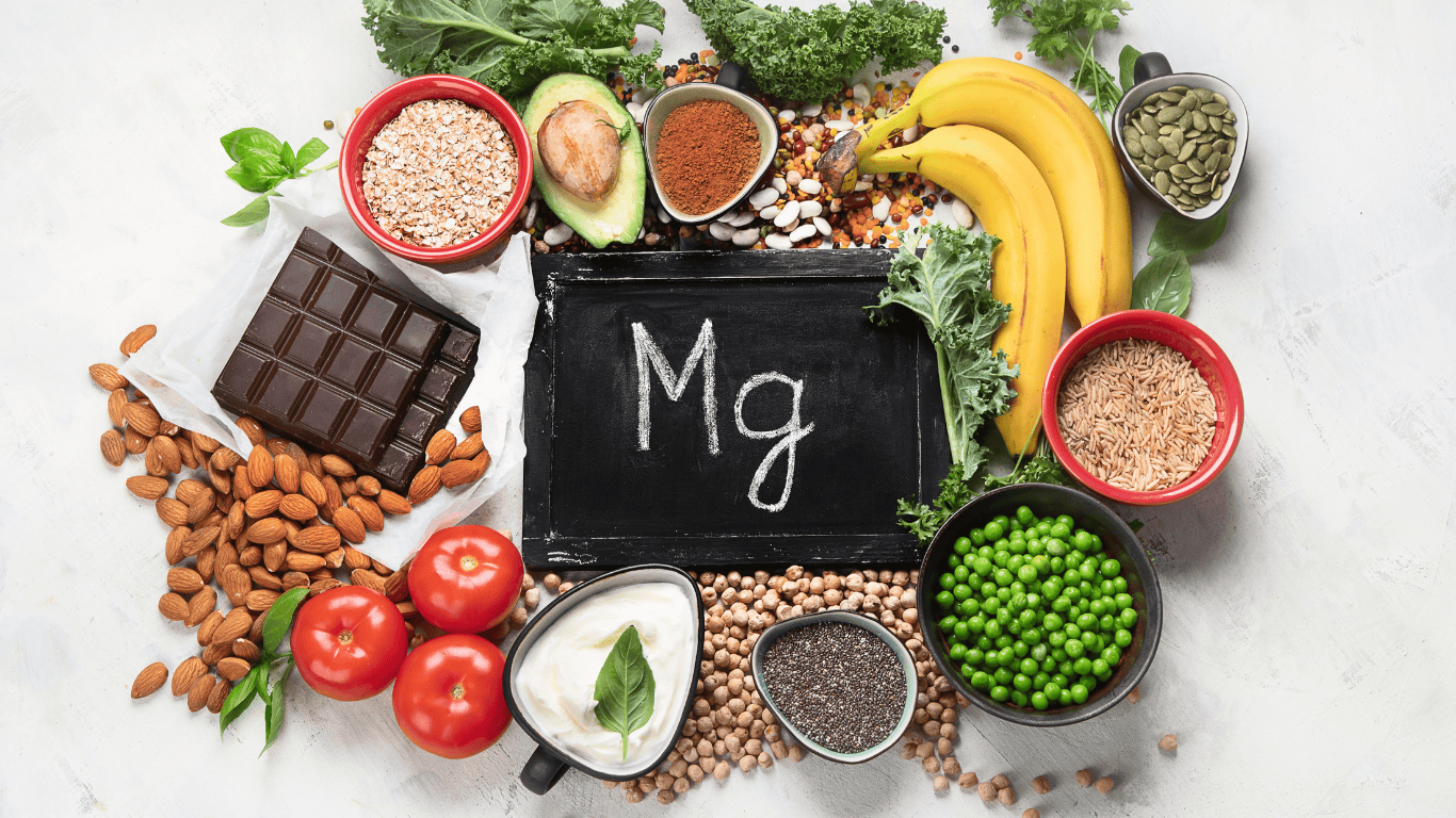 Comida como plátanos, tomates, legumbres, guisantes, chocolates esparcidos en una mesa con las siglas Mg en medio, de magnesio