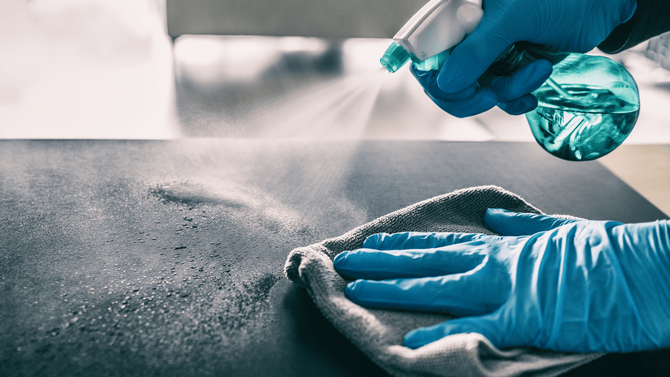 Persona desinfectando una mesa con un trapo, guantes y spray